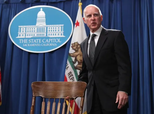 حاكم كاليفورنيا غافين نيوسوم يقف أمام منصة تحمل شعار الولاية، مستعدًا لمناقشة قرارات الإفراج المشروط للأخوين مينينديز.