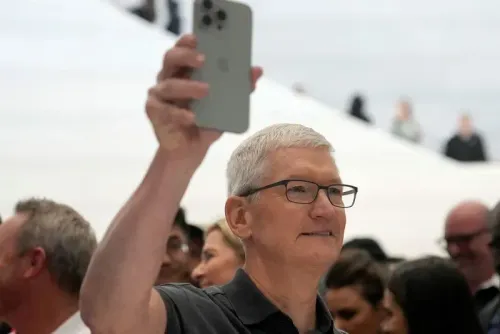 تيم كوك، الرئيس التنفيذي لشركة آبل، يحمل هاتف آيفون خلال حدث إطلاق، مع جمهور خلفه، في إشارة إلى التغييرات المحتملة في الأسعار.