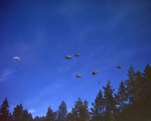 مجموعة من المظليين أثناء القفز بالمظلات فوق غابة، في سياق تاريخي يتعلق بمهمة إخماد حرائق الغابات خلال الحرب العالمية الثانية.