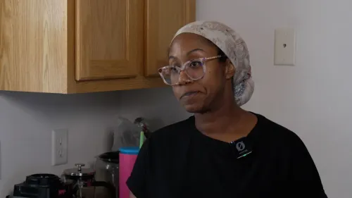 امرأة ترتدي حجابًا وتظهر علامات القلق في وجهها، بينما تتحدث عن تحديات تأمين الغذاء لأطفالها في ظل ضغوط مالية.