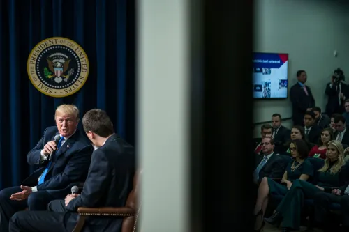 تشارلي كيرك يتحدث مع الرئيس ترامب خلال حدث في البيت الأبيض، مع وجود جمهور من الحضور خلفهم.