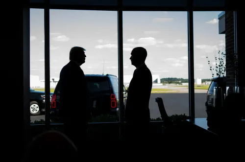 صورة تظهر ظلال كريستي نويم وكوري ليفاندوفسكي في مطار، مع خلفية تضم سيارات ومشهد السماء، تعكس تأثير ليفاندوفسكي في وزارة الأمن الداخلي.