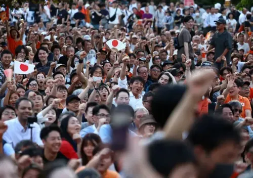 حشد كبير من الأشخاص في تجمع سياسي لحزب سانسيتو في اليابان، يحملون أعلامًا ويعبرون عن حماسهم.