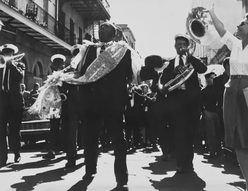 موكب موسيقي في شوارع نيو أورلينز يضم عازفين يرتدون ملابس رسمية، يحتفلون بحياة الراحلين في تقليد الصف الثاني الجنائزي.