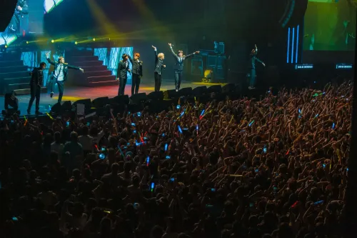 فرقة BTS تؤدي أمام حشد كبير من المعجبين في حفل موسيقي، مع أضواء ملونة وأجواء احتفالية تعكس شغف الكيبوب في أمريكا اللاتينية.