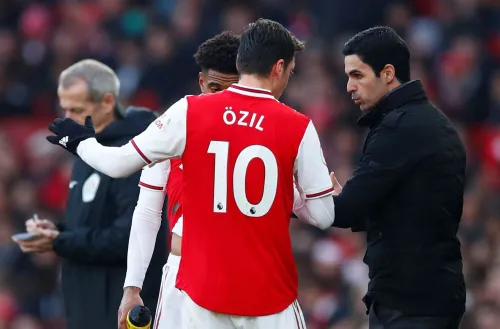 مشهد لمباراة Arsenal حيث يتحدث المدرب Mikel Arteta مع اللاعب Mesut Özil، مع التركيز على تكتيكات الفريق وأهمية التواصل بينهما.