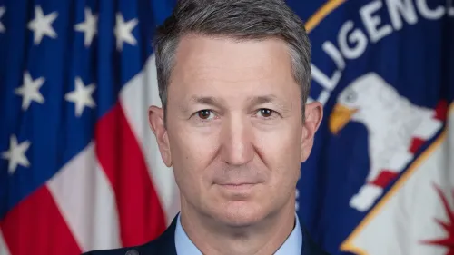 الجنرال المتقاعد جون كاين، طيار محترف في سلاح الجو الأمريكي، يرتدي زياً رسمياً أمام علم الولايات المتحدة، بعد تعيينه رئيساً لهيئة الأركان المشتركة.