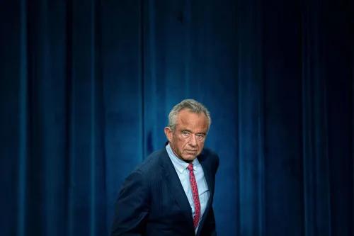 روبرت كينيدي جونيور، وزير الصحة والخدمات الإنسانية، يبدو جادًا أثناء حديثه في مؤتمر، مع خلفية زرقاء.