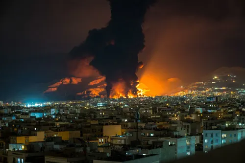 دخان كثيف يتصاعد من منطقة جبلية مضاءة بالنيران، مع خلفية لمدينة مضاءة ليلاً، مما يعكس تأثير الحرب على إمدادات النفط.