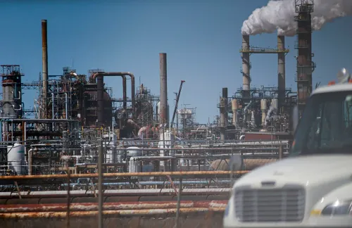 مصنع للنفط مع أنابيب ضخمة وأبراج تدخين، يعكس التحديات البيئية المرتبطة بالوقود الأحفوري وتأثيرها على المناخ.