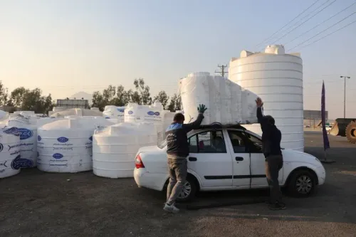 عمال يقومون بتحميل خزانات مياه بلاستيكية على سيارة في موقع تخزين، وسط أزمة مياه حادة في إيران.