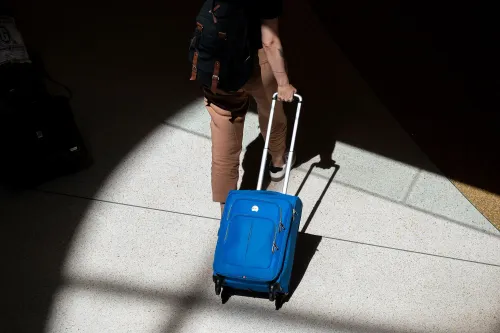 شخص يسير في مطار مع حقيبة سفر زرقاء، مما يعكس استعداد الأمريكيين للسفر في عطلة نهاية الأسبوع الأخيرة من الصيف.