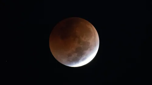 القمر أثناء خسوفه الكلي، يظهر بلون نحاسي مائل إلى الحمرة، في ظلام السماء، مع تداخل الظل على جانبه.