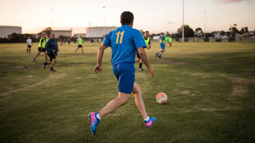 رجل يرتدي قميصًا أزرق يحمل الرقم 11، يركض في ملعب كرة القدم مع مجموعة من اللاعبين الآخرين، مما يعكس أهمية الأنشطة الاجتماعية في تحسين التوازن بين العمل والحياة.