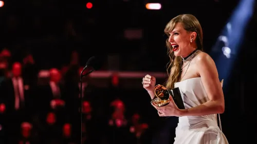 تظهر الصورة فنانة مشهورة تحتفل بفوزها بجائزة جرامي، مرتدية فستاناً أنيقاً وتبتسم بسعادة، مع جمهور خلفها.