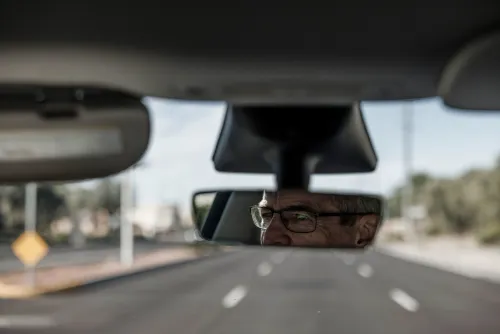صورة تظهر رجلًا مسنًا يرتدي نظارات، ينظر إلى المرآة الخلفية في السيارة، مع طريق فارغ في الخلفية، مما يعكس شعورًا بالترقب بشأن مراكز البيانات في تشاندلر.