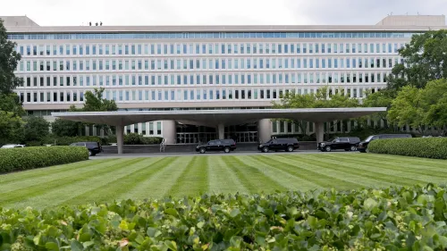 مبنى وكالة الاستخبارات المركزية يظهر في الصورة، مع سيارات سوداء متوقفة أمام المدخل. الصورة تعكس التوترات حول تقليص القوى العاملة.