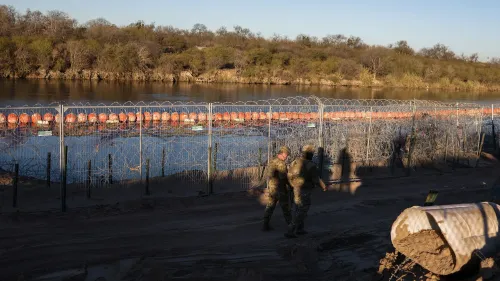 صورة لجنود يسيرون بجوار سياج شائك على الحدود الأمريكية المكسيكية، حيث تظهر العوائق المائية المستخدمة للحد من الهجرة غير القانونية.