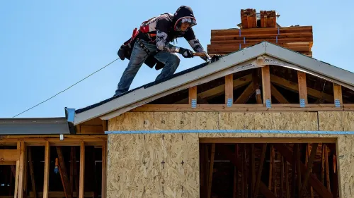 عامل بناء يعمل على تركيب السقف في مشروع إنشاء منزل جديد، مع التركيز على التحديات الحالية في سوق العمل الأمريكي.