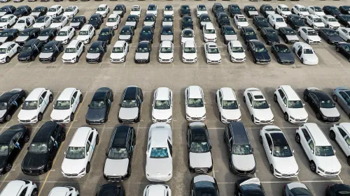 صف من السيارات الجديدة باللونين الأسود والأبيض في موقف سيارات واسع، يعكس تأثير الرسوم الجمركية على صناعة السيارات الأمريكية.