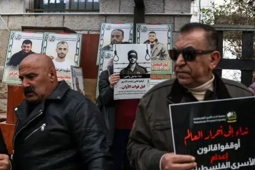 محتجون فلسطينيون يحملون لافتات وصور أسرى خلال مظاهرة ضد قانون الإعدام الجديد في الضفة الغربية، مع شعارات تدعو للتضامن.