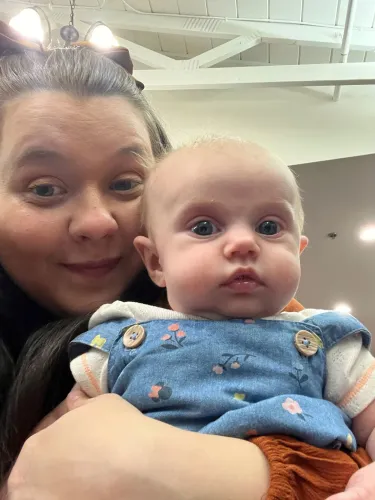 امرأة تحمل طفلاً صغيرًا في حضنها، مع تعبيرات وجه تعكس الحنان والارتباط، في سياق الحديث عن تحديات الأسر ذات الدخل المنخفض.