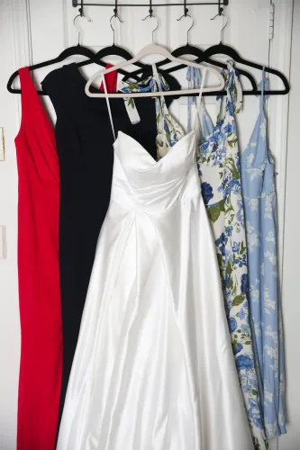 مجموعة من الفساتين المعلقة، تشمل فستان زفاف أبيض وألوان متنوعة، تعكس تنوع الملابس الرسمية المستخدمة في حفلات الزفاف.