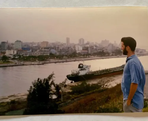 رجل يقف على ضفة نهر في هافانا، كوبا، مشرفًا على المدينة والسفينة الراسية، مما يعكس أجواء تاريخية وثقافية غنية.