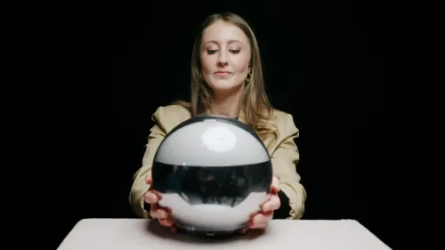 امرأة تحمل كرة فضية تعكس الضوء، بينما تجلس أمام خلفية داكنة، تشير إلى تقنية التحقق من الهوية باستخدام Orb.