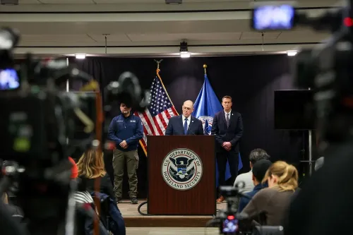 مؤتمر صحفي حول قضايا الهجرة في مينيسوتا، يظهر فيه مسؤولون من إدارة الأمن الداخلي، مع العلم الأمريكي وشعارات الوكالة.