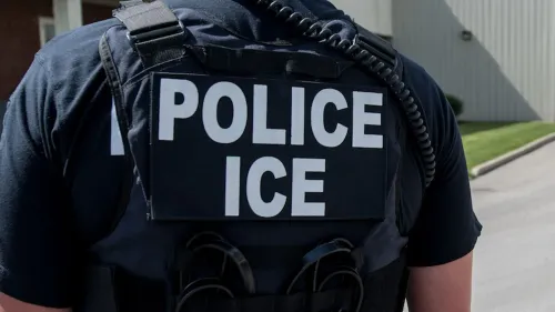 شخص يرتدي سترة سوداء تحمل عبارة "شرطية ICE" مع سماعة أذن، في منطقة بالقرب من مدرسة ابتدائية في شيكاغو.