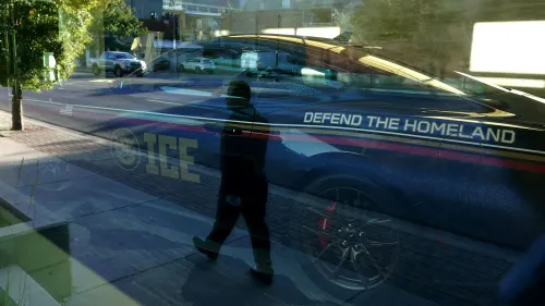 صورة تعكس ضابطًا يمشي بجانب سيارة تابعة لوكالة إنفاذ قوانين الهجرة والجمارك، مكتوب عليها "دافع عن الوطن".