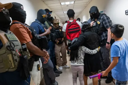 عناصر من قوات إنفاذ قوانين الهجرة والجمارك تتواجد في ممر، بينما تحتضن عائلة أطفالها في حالة من القلق والخوف.