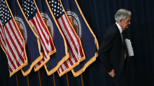 رجل مسن يرتدي بدلة رسمية يسير بجوار أعلام الولايات المتحدة، مع التركيز على التوترات الاقتصادية وتأثيرها على قرارات الاحتياطي الفيدرالي.