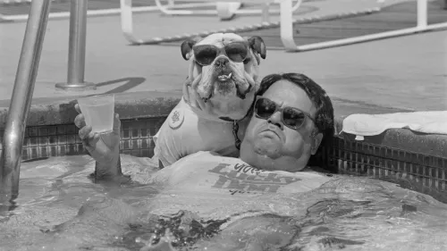 رجل يرتدي نظارات شمسية يجلس في حوض سباحة مع كلب بولدوغ يرتدي نظارات شمسية أيضًا، يجسد علاقة مريحة وممتعة بين الإنسان والحيوان.