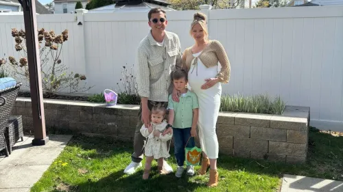 عائلة مكونة من أربعة أفراد، تتضمن أم حامل وطفلين، يقفون في حديقة ذات خلفية بيضاء، يحتفلون بلحظة عائلية سعيدة.