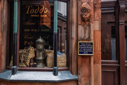 واجهة مقهى تاريخي في لندن، تعرض لافتة تشير إلى أول مقهى في المدينة، مع تفاصيل عن القهوة والتقاليد الثقافية.