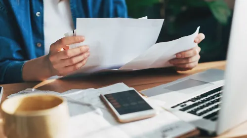 شخص يراجع فواتير طبية وأوراق مالية على طاولة، مع وجود هاتف محمول ولاب توب، مما يعكس قلق المستهلكين حول الديون الطبية وتأثيرها على الائتمان.