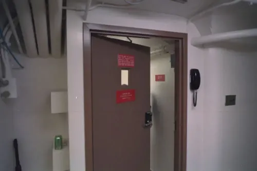 باب مدخل ملجأ سري تحت الأرض في البيت الأبيض، مع لافتات تحذيرية، يرمز إلى تاريخ البناء السري والتطورات الأمنية.