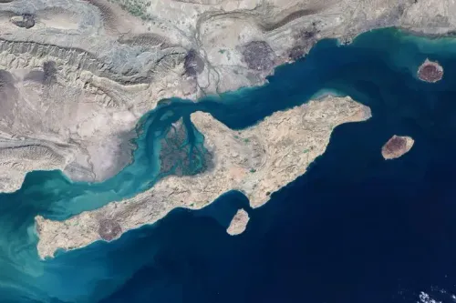 صورة جوية لجزيرة قشم في مضيق هرمز، تُظهر تضاريسها الطبيعية وتداخل المياه الزرقاء مع اليابسة، تعكس أهميتها الاستراتيجية.