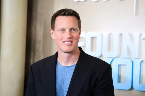 ديفيد إليسون، الرئيس التنفيذي الجديد لشركة باراماونت، مبتسم أثناء ظهوره في حدث رسمي، مع خلفية تحمل اسم الشركة.