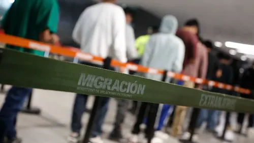 طابور من المهاجرين في مركز للترحيل، مع وجود شريط يفصل بينهم يحمل كلمة "هجرة" باللغتين الإسبانية والإنجليزية.