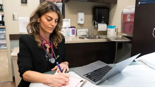 طبيبة تعمل في عيادة، تسجل ملاحظات على دفتر، مع جهاز كمبيوتر محمول وأدوات طبية حولها، في سياق تفشي الحصبة في تكساس.