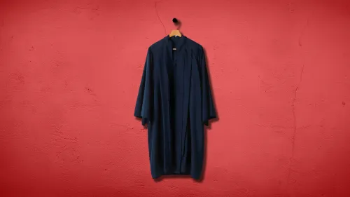 عباءة قاضي هجرة معلقة على شماعة أمام جدار أحمر، تعكس التحديات التي تواجه محاكم الهجرة في ظل التغيرات السياسية.