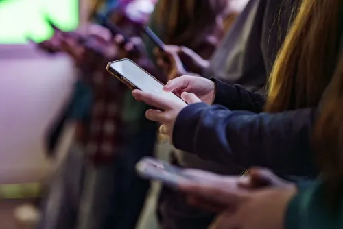 أيدي مراهقين تحمل هواتف ذكية في بيئة مضاءة بشكل خافت، تعكس تأثير إنستجرام على الشباب وتحديثات الأمان الجديدة.