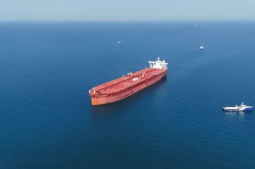 سفينة شحن كبيرة تبحر في مياه مضيق هرمز، مع وجود قوارب حربية إيرانية قريبة، في ظل توترات متزايدة حول حرية الملاحة.