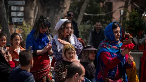 نساء يرتدين ملابس تقليدية ملونة في مناسبة ثقافية، مع التركيز على التعبيرات الجادة أثناء التفاعل مع الأحداث.