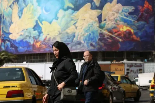 امرأة ترتدي الحجاب تسير في الشارع أمام لوحة جدارية ملونة، بينما يقف رجل خلفها، مع سيارات الأجرة في الخلفية.