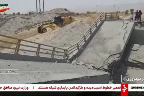 جسر مدمر في منطقة صحراوية مع وجود آليات ثقيلة وأشخاص في الخلفية، يعكس تأثير الضربات الأمريكية على البنية التحتية في إيران.