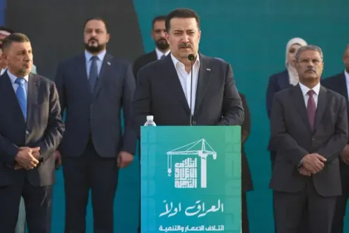 رئيس الوزراء العراقي محمد شياع السوداني يتحدث خلال فعالية انتخابية، محاطًا بعدد من المسؤولين، مع شعار تحالف البناء والتنمية خلفه.